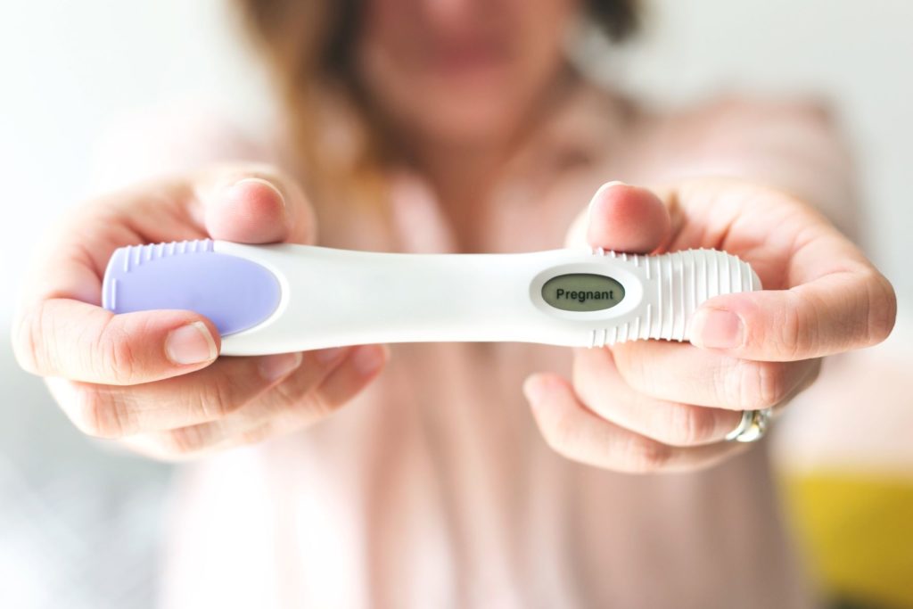 Woman holding a positive pregnancy test in front of her.